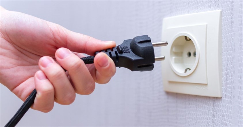  Tangan seseorang memegang colokan listrik, menunjukkan pentingnya mencabut kabel saat tidak dipakai untuk hemat listrik.