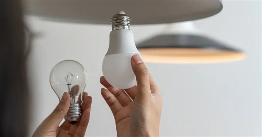 Seseorang memegang lampu LED hemat energi di tangan, menunjukkan cara mengganti lampu biasa dengan lampu LED.