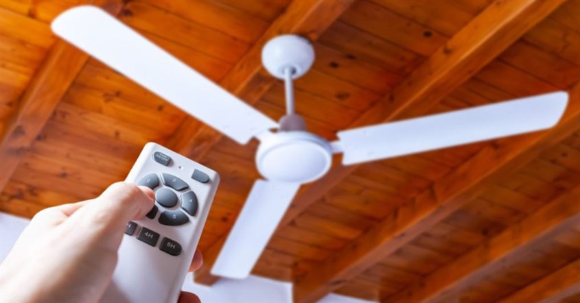  Orang memegang remote control di atas kipas langit-langit, menunjukkan cara hemat listrik dengan mematikan alat.